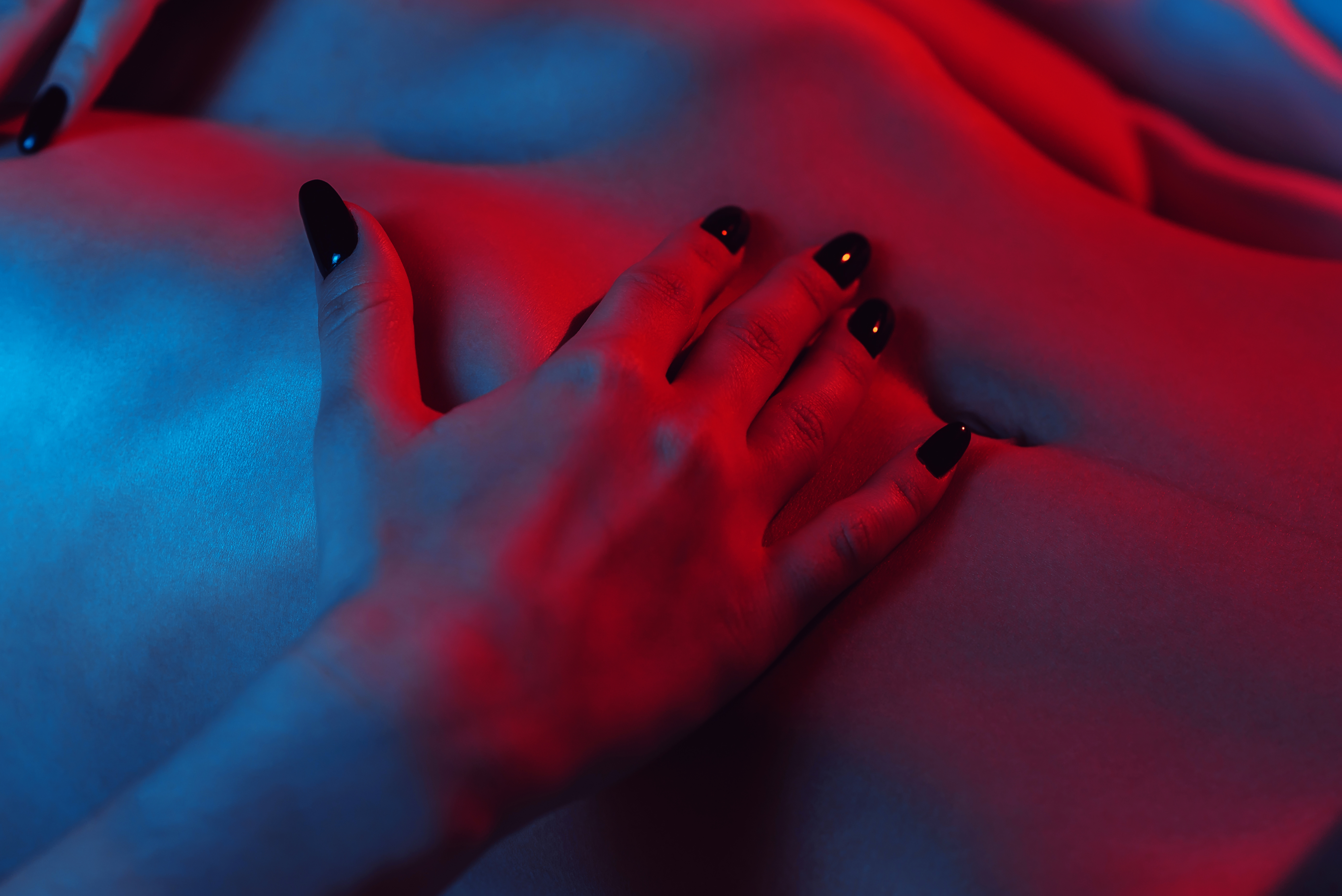 woman hand on a slender tummy close-up with red-blue neon lighting. Soft focus